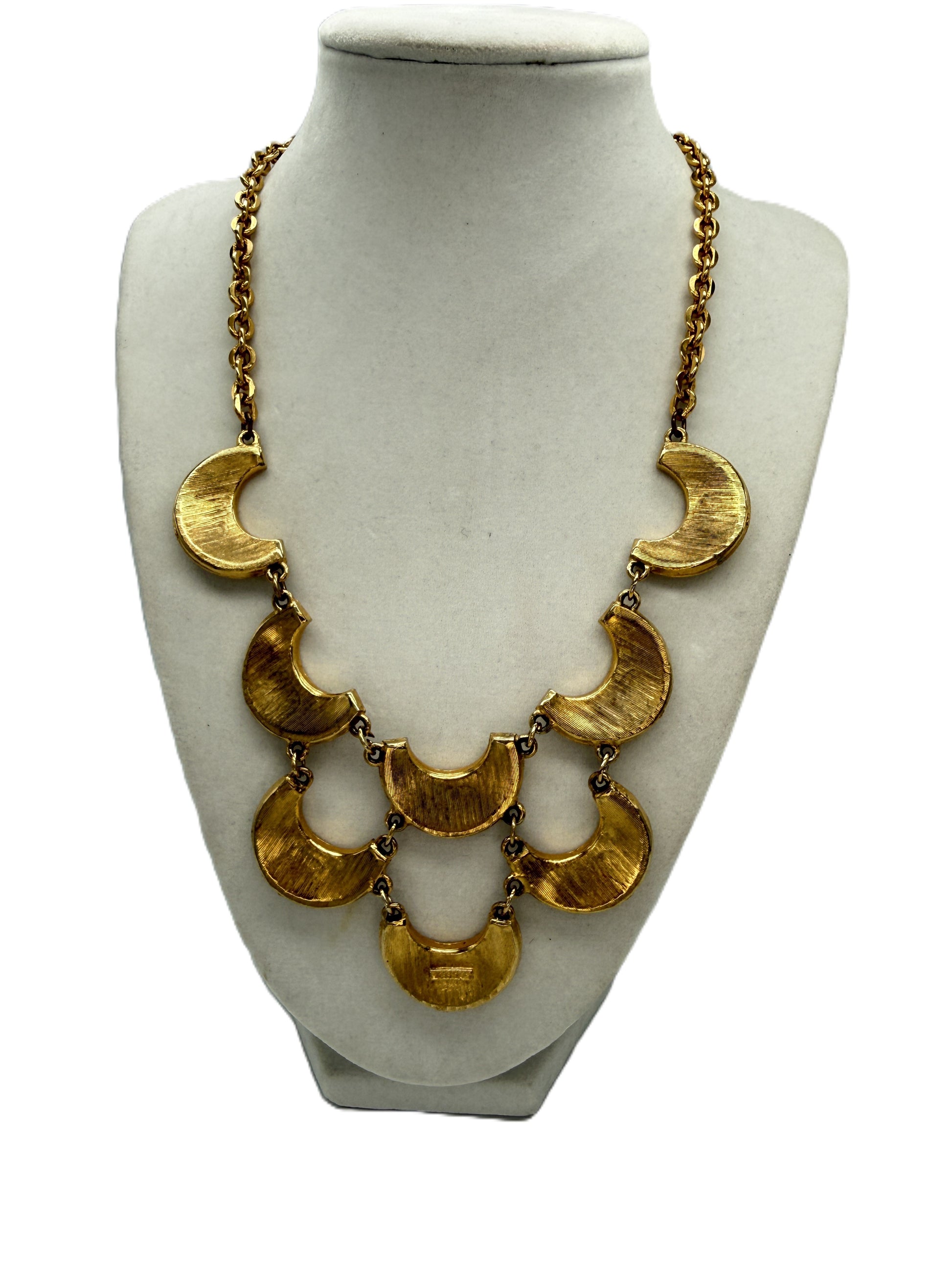A gold statement necklace with multiple crescent moon and semi-circular links, displayed on a white fabric mannequin bust against a white background.
