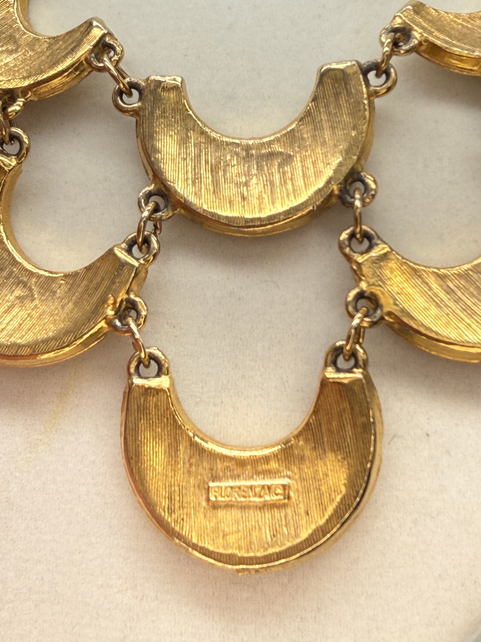 Close-up of a gold-tone metal link chain necklace with crescent-shaped links on a light beige background signed Florenza.