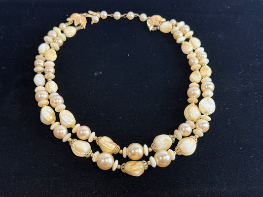 A multi-strand vintage Trifari pearl necklace with gold-toned metal accents, displayed on a dark black background.