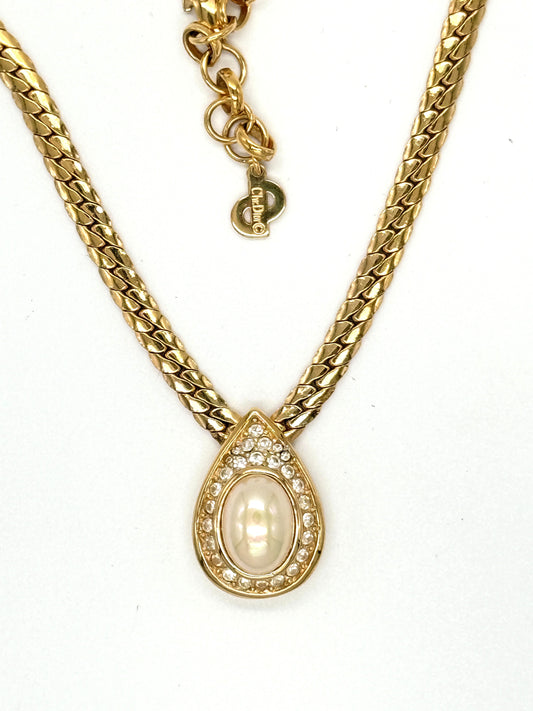 A gold chain necklace featuring a teardrop-shaped pendant with a central cream-colored pearl surrounded by small clear rhinestones, signed Christian Dior vintage.